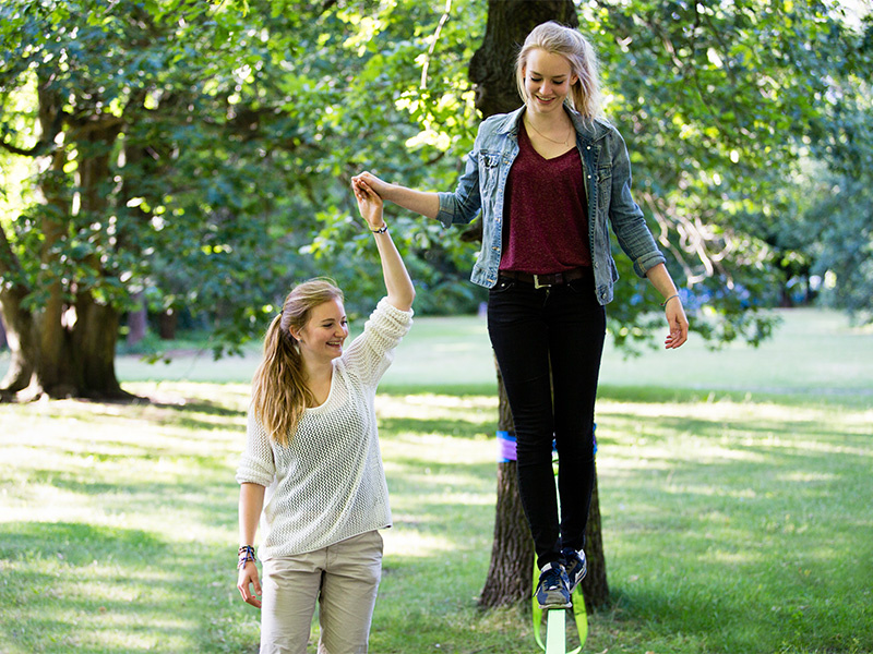 Outdoor-Sport-Trend: Slacklinen Beim Slacklinen balancierst du auf einem dehnbaren Gurtband, das zwischen 2 Ankerpunkten (z. B. Bäumen) fixiert wird.