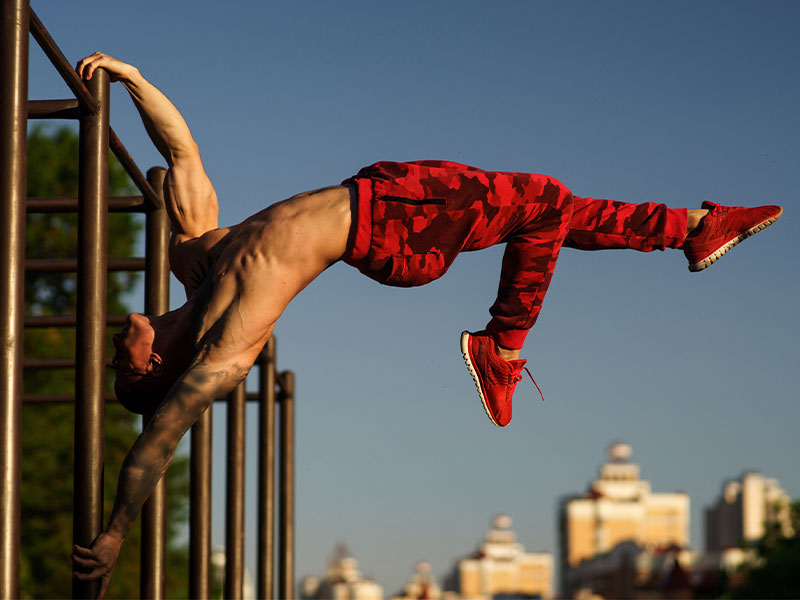 Calisthenics-Übung: One Leg Flag Hänge dich in die Ausgangsposition der Human Flag und ziehe dein oberes Bein angewinkelt zum Körper. Strecke dein unteres Bein nach oben durch.