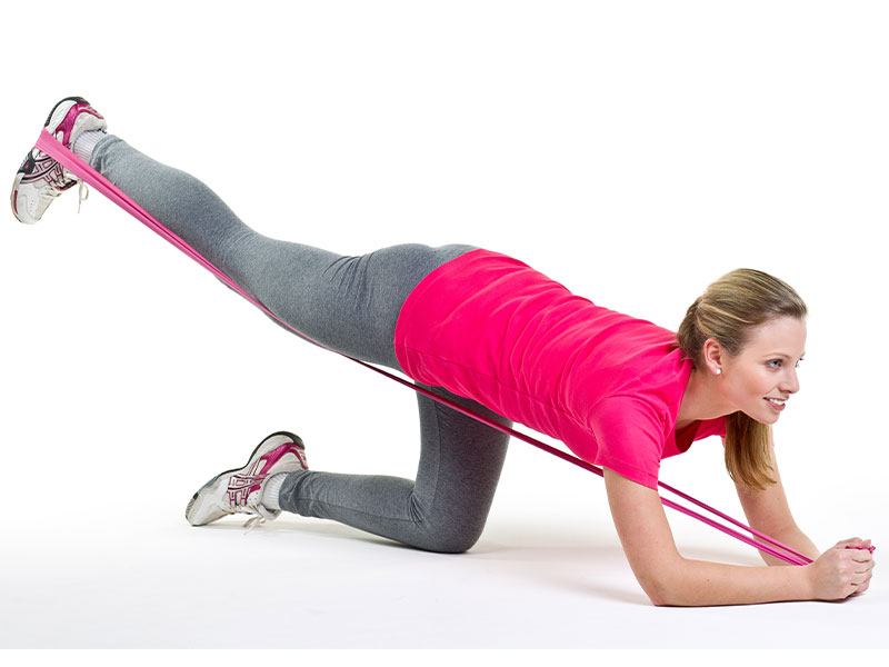 Fitness First Expert:innen-Tipp für den Knack-Po: Kickbacks mit Theraband Junge Frau macht Kickbacks mit Theraband für den Po im Home Workout.