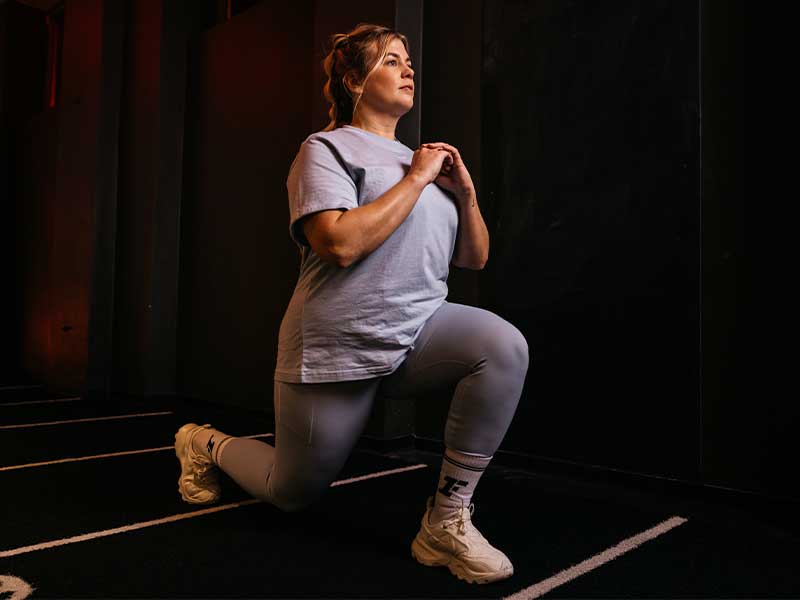 Geh‘ in einen Ausfallschritt. Hinteres und vorderes Bein sind 90 Grad gebeugt. Halte deinen Oberkörper dabei gerade. Dein hinteres Knie ist knapp über dem Boden.