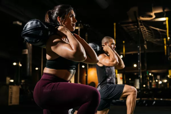 Junges Paar macht Ausfallschritte mit Sandsack.