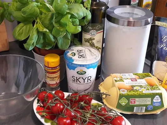 250 g Skyr Natur, 80 ml Olivenöl, 80 ml Milch, 2 Eier (Größe M), 300 g Mehl, 2 TL Backpulver, 4 Zweige Rosmarin, 10 Stiele Thymian, 100 g Parmesan, 250 g Kirschtomaten, 12 Scheiben Parmaschinken.