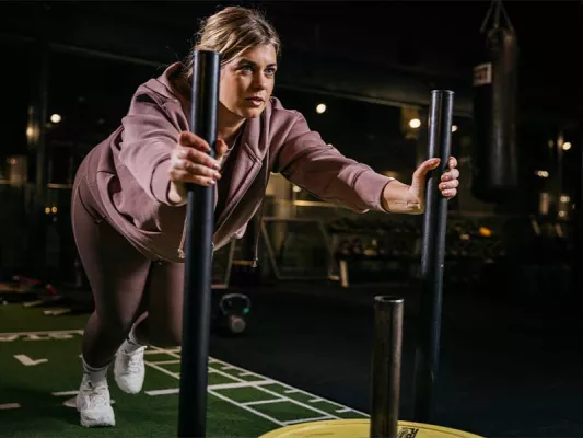 Frau schiebt Gewichtsschlitten beim Hyrox-Training bei Fitness First