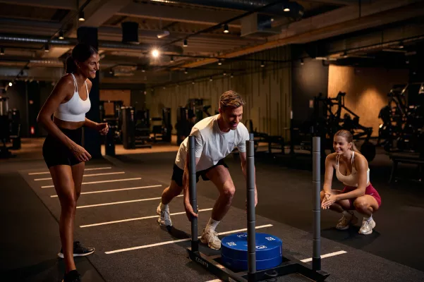 Junger Mann wird beim Sled Push von 2 jungen Frauen angefeuert.